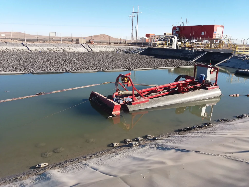 Draga LWT no tripulada de FreeMAQ realizando dragado remoto en una piscina industrial con geomembrana HDPE para recuperación de capacidad de almacenamiento.