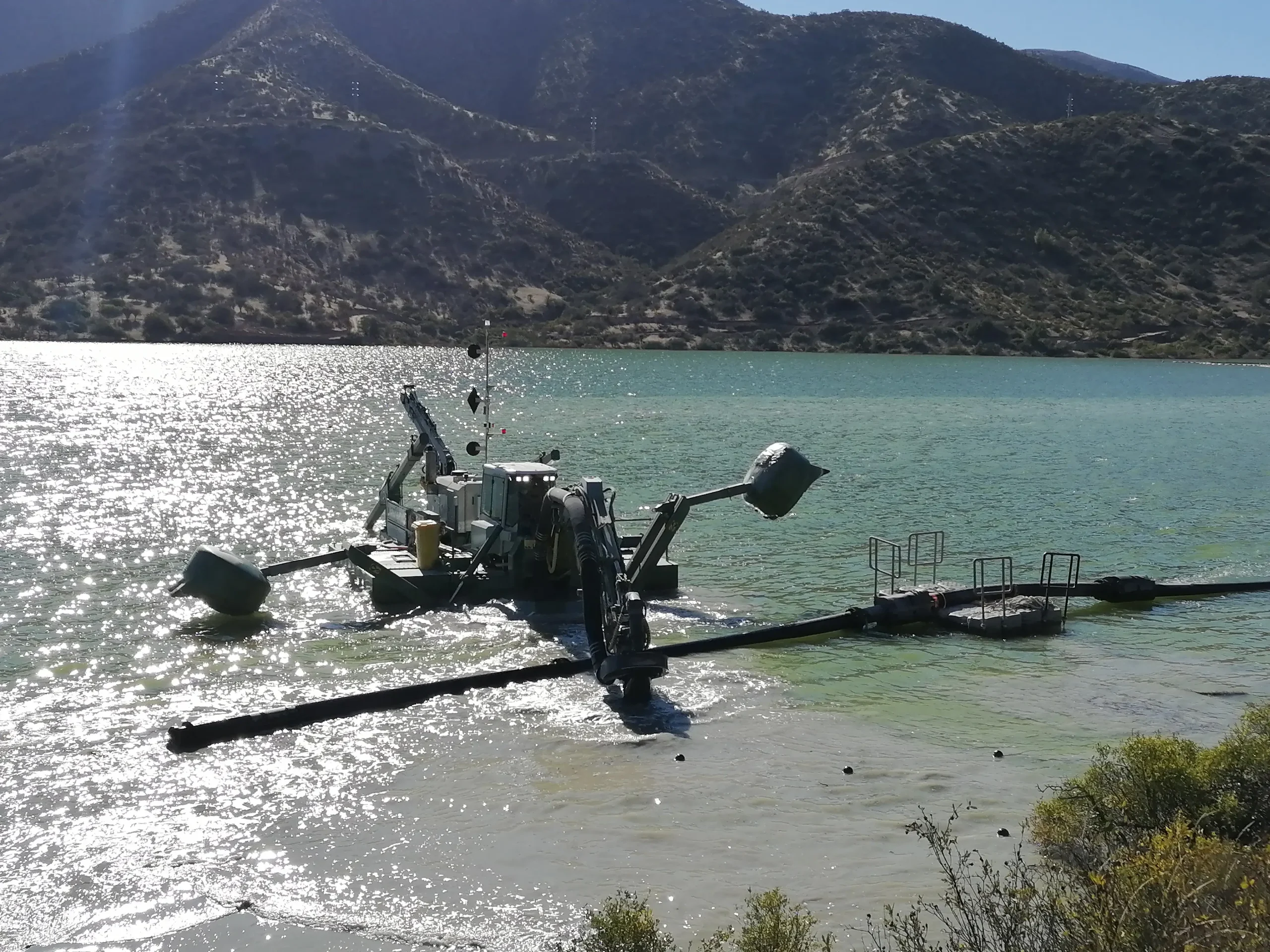 Draga anfibia operando en un embalse asociado a una central hidroeléctrica para el control y extracción de sedimentos acumulados.